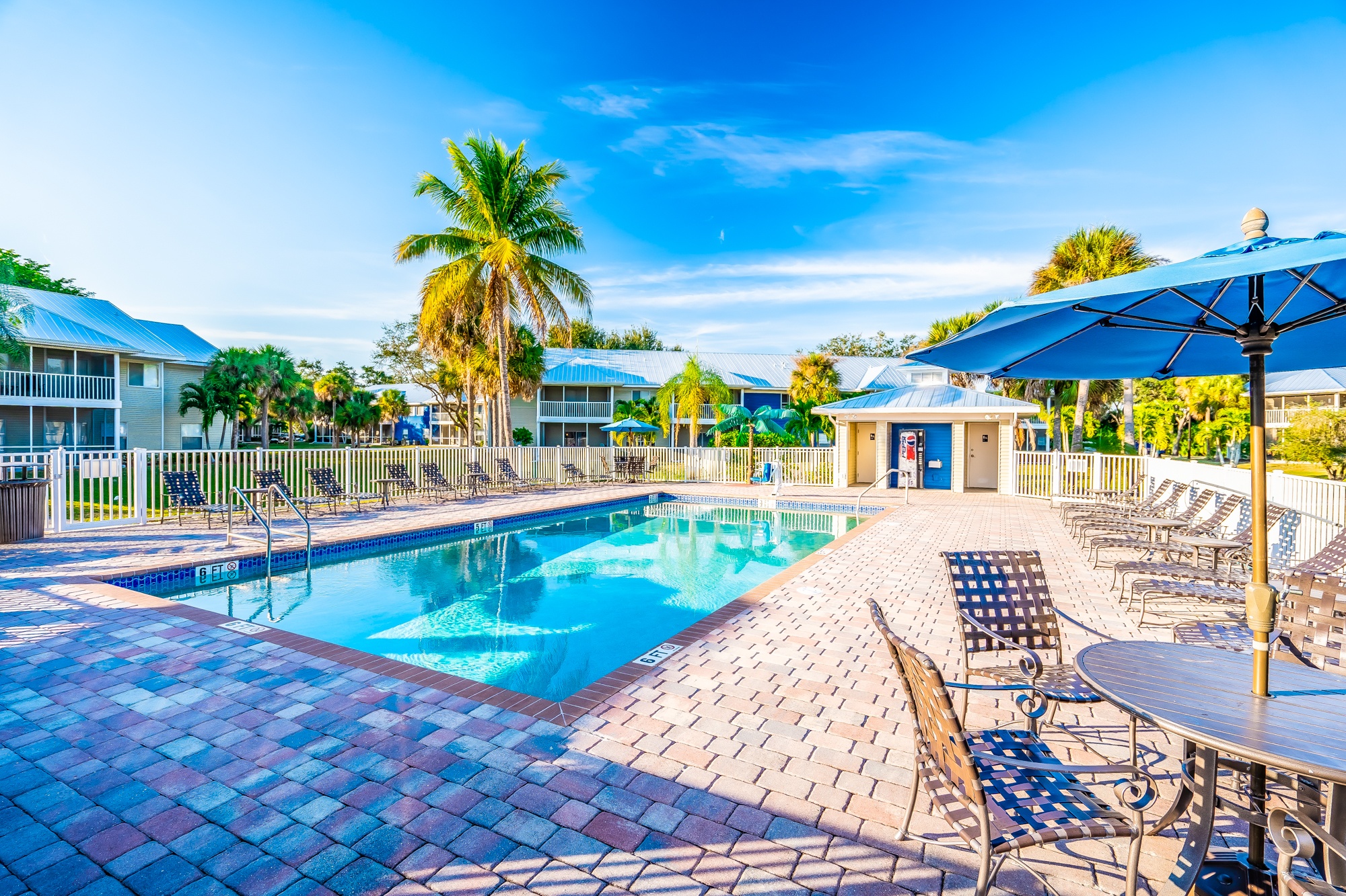 A pool surrounded by chairs and umbrellas with a building in the background.